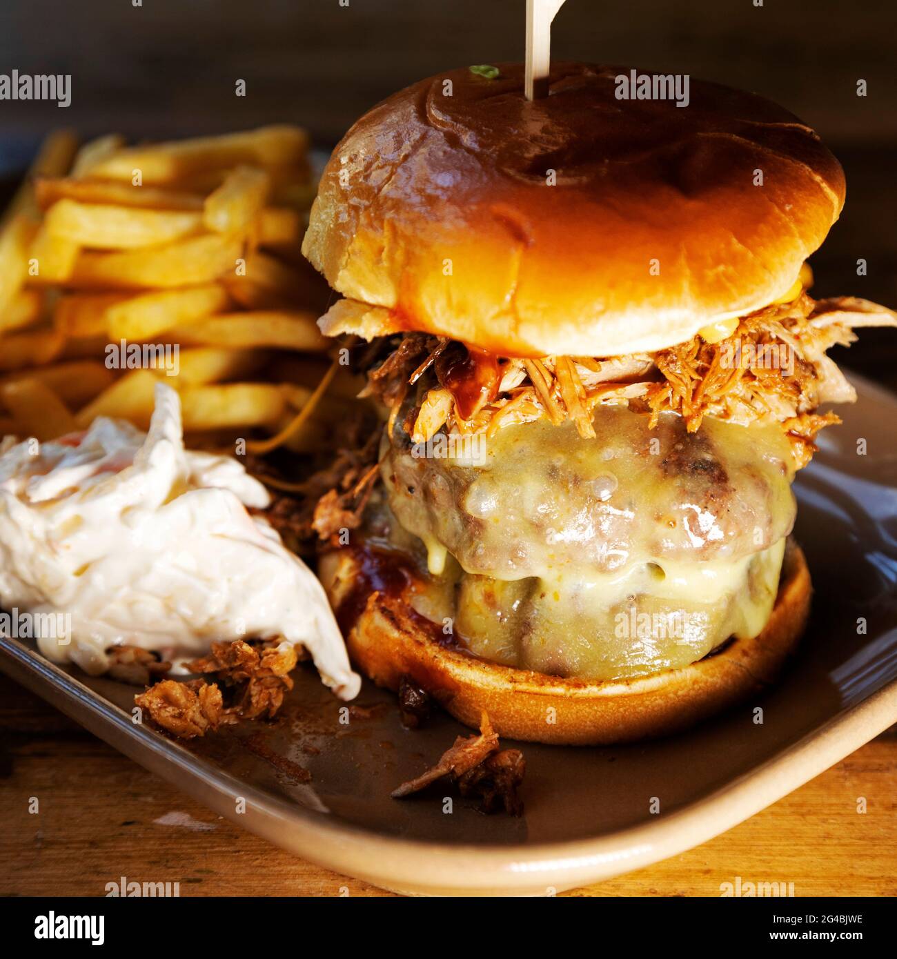 Hamburguesa en un bollo brioche servido con fritos y 'slaw. La hamburguesa está cubierta con queso derretido y carne de cerdo desmenuzada. Foto de stock