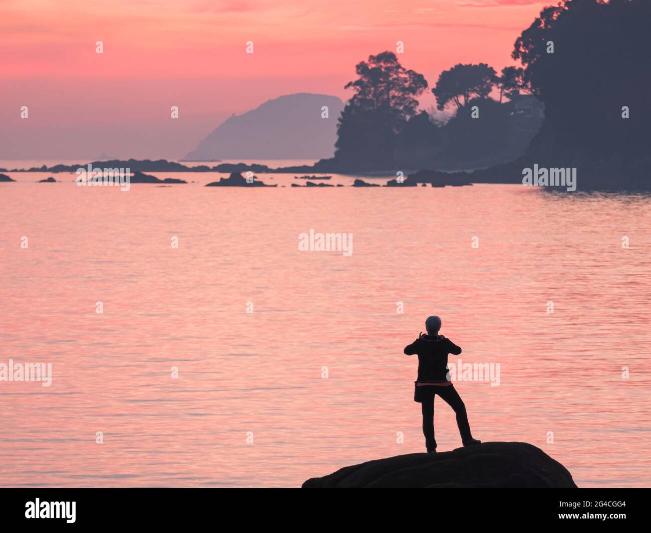persona irreconocible haciendo fotos con móvil al atardecer en una roca a las islas cíes en españa Foto de stock