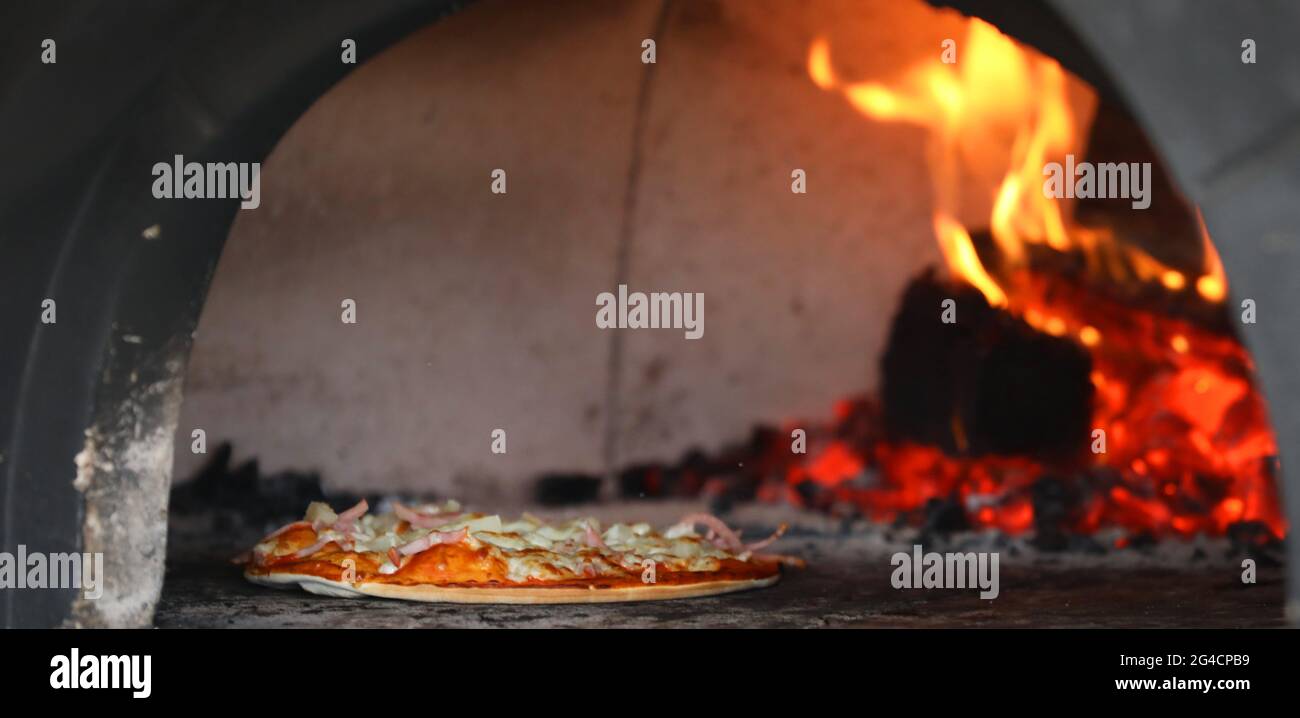 Vista al interior de un auténtico horno de leña con una pizza tradicional cocinando dentro de él. Interior de horno de pizza con llamas, caldos y madera. Foto de stock