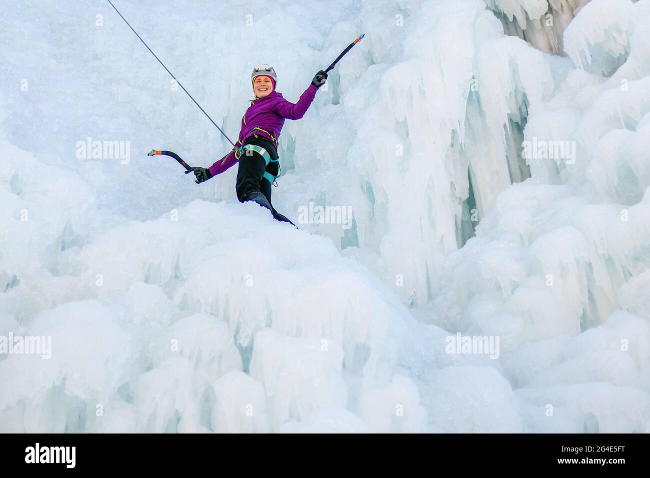 Escalador de hielo hembra en posición de tracción, haciendo pivotar los ejes de hielo sobre la cabeza y plantando la pick en el hielo, vista lateral Foto de stock