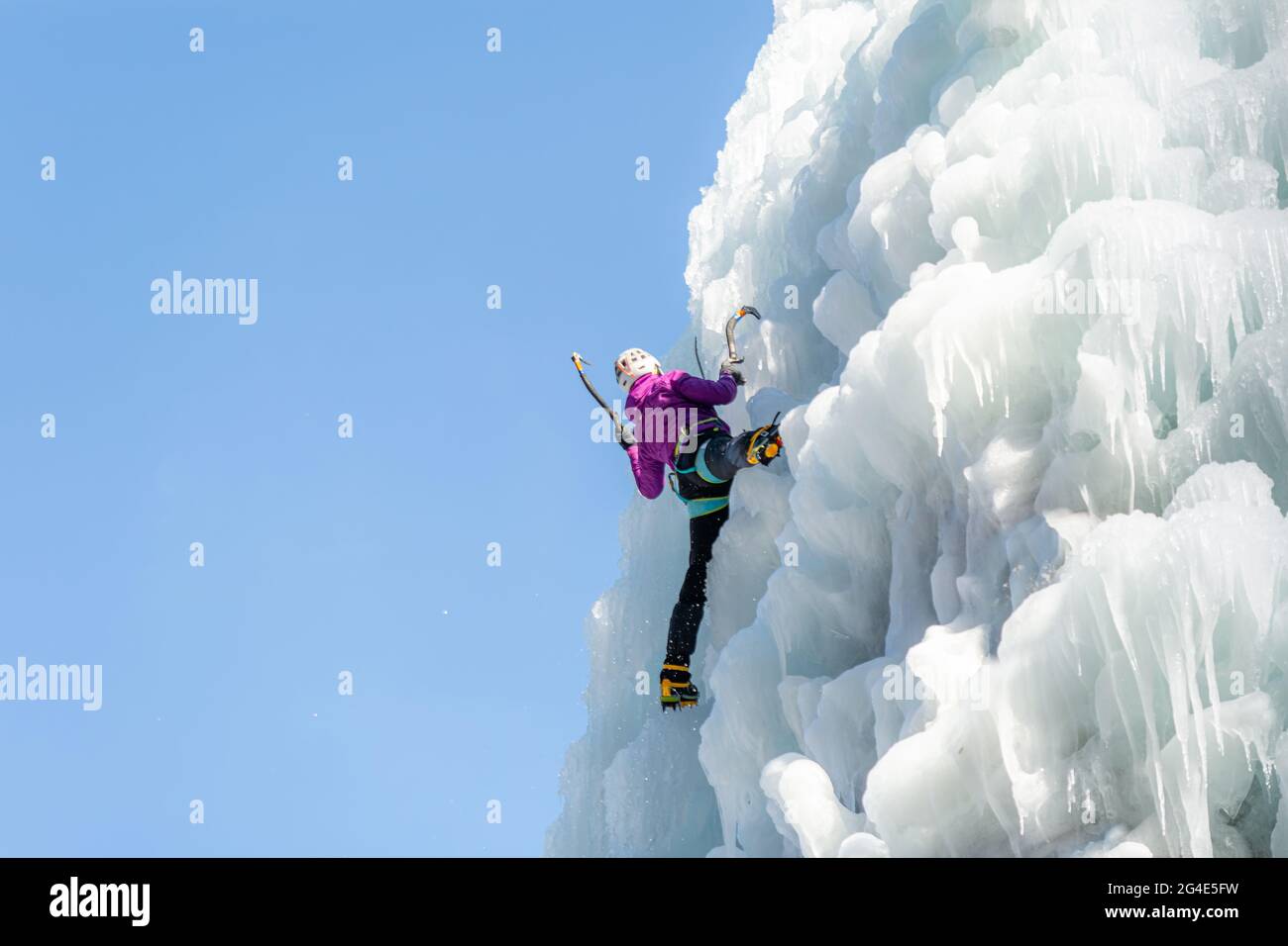 Escalador de hielo hembra en posición de tracción, haciendo pivotar los ejes de hielo sobre la cabeza y plantando la pick en el hielo, vista lateral Foto de stock