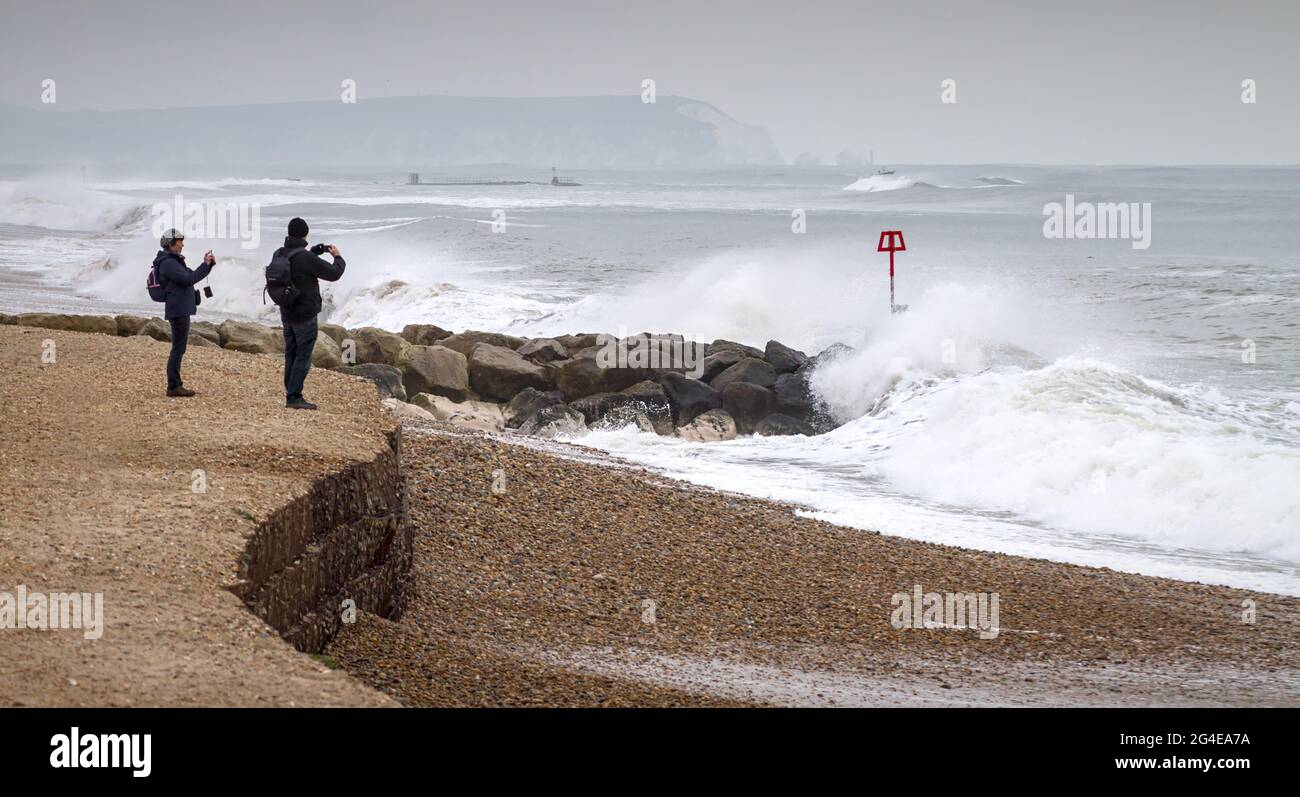 Dos, Par, gente fotografiando olas pesadas que rompen en la playa de Hengistbury Head durante una tormenta en invierno con agujas y la isla de Wight en el Distán Foto de stock