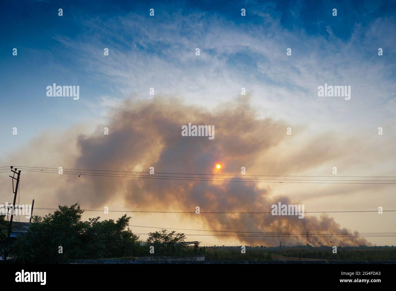 Humo saliendo de las fábricas En el horizonte, la contaminación del aire se está extendiendo como nubes y cubriendo el sol poniente. Rodada en la aldea rural de WB, India. Foto de stock