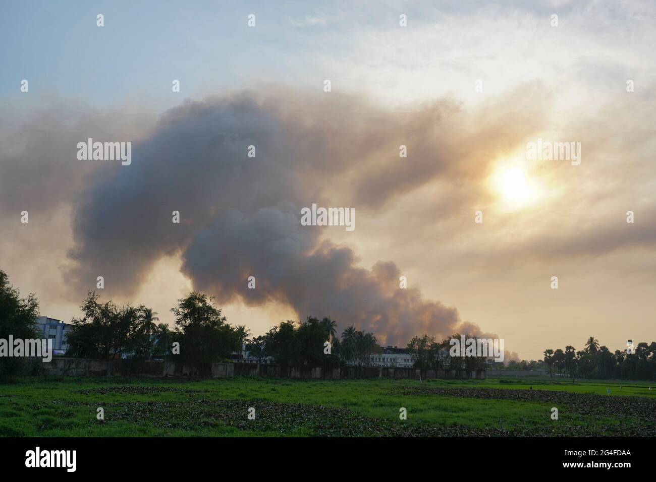 Humo saliendo de las fábricas En el horizonte, la contaminación del aire se está extendiendo como nubes y cubriendo el sol poniente. Rodada en la aldea rural de WB, India. Foto de stock