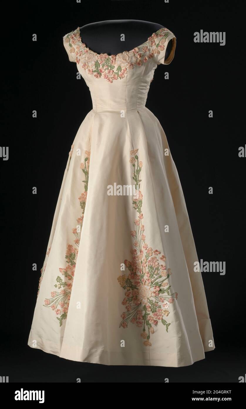 Un vestido de seda color crema con aplique floral bordadoé  decoraciones diseñadas por Ann Lowe. El vestido tiene un corpiño con mangas  casquillo, un cuello redondo en la parte delantera y una