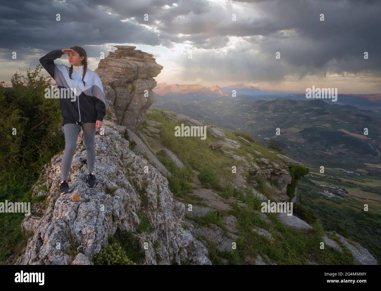 Mujer con chubasquero en el borde de un acantilado con vistas a un valle en un día lluvioso y húmedo. Imagen conceptual de tonos exteriores.Torcal de Antequera,España. Foto de stock