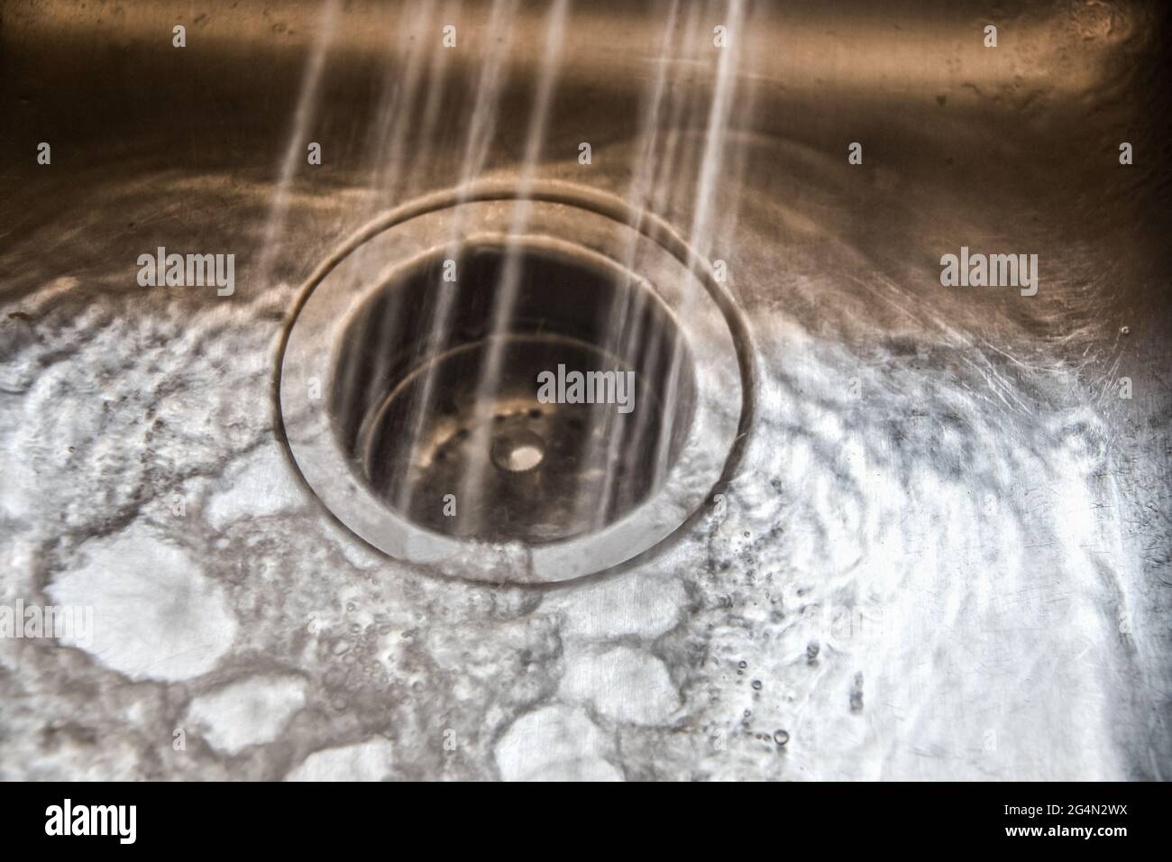 Agua monocromática pulverizada en un depósito de basura en un fregadero de acero inoxidable con agua y burbujas que se juntan y se ejecutan en la superficie - algunos granos y mo Foto de stock