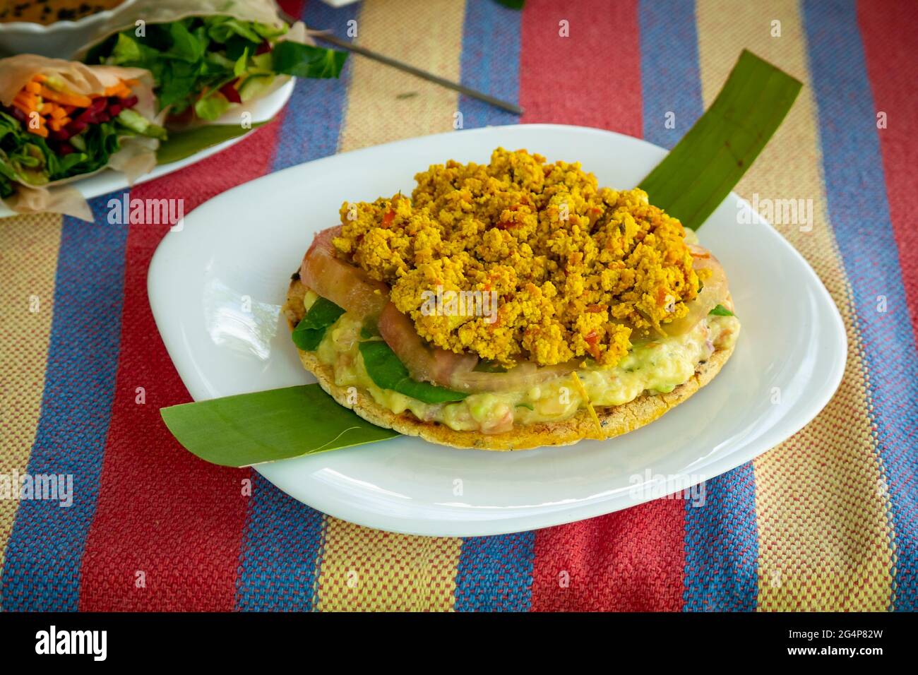 Aperitivo típico colombiano Arepa relleno con tomate, aguacate y tofu servido en un plato blanco Foto de stock