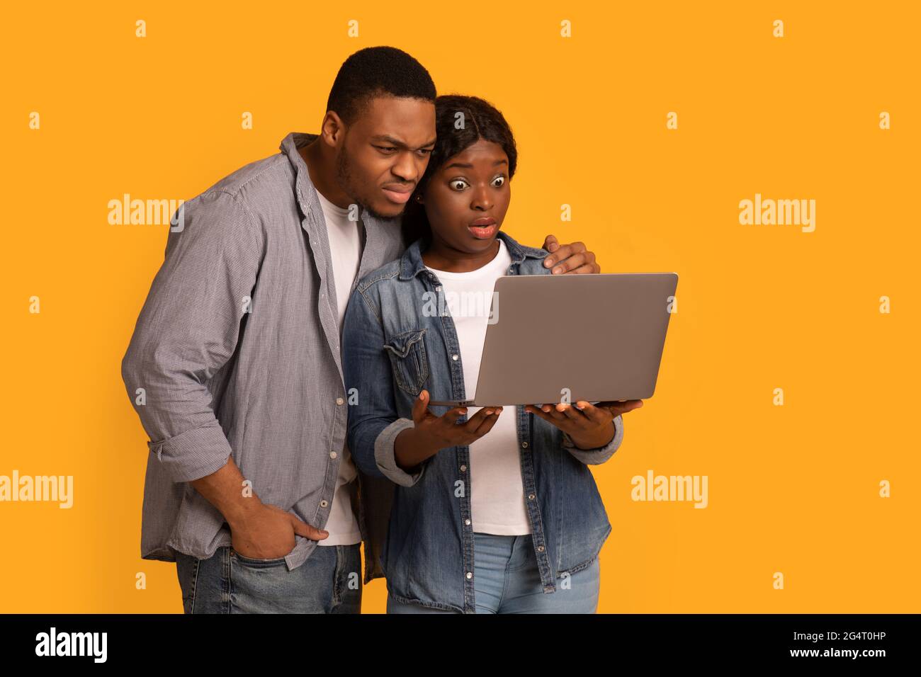 Contenido de choque. Abrumados African American Couple mirando a la pantalla del ordenador portátil, el hombre negro joven y la mujer sosteniendo la computadora, sufriendo de estafa del Internet Foto de stock