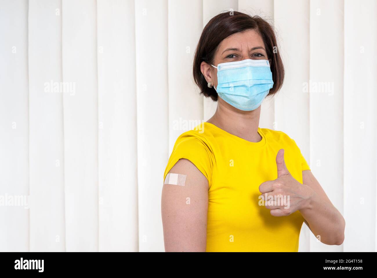 Retrato de una mujer en máscara quirúrgica que gestora pulgares para arriba después de ser vacunado contra coronavirus. Vacuna Covid-19. Foto de stock
