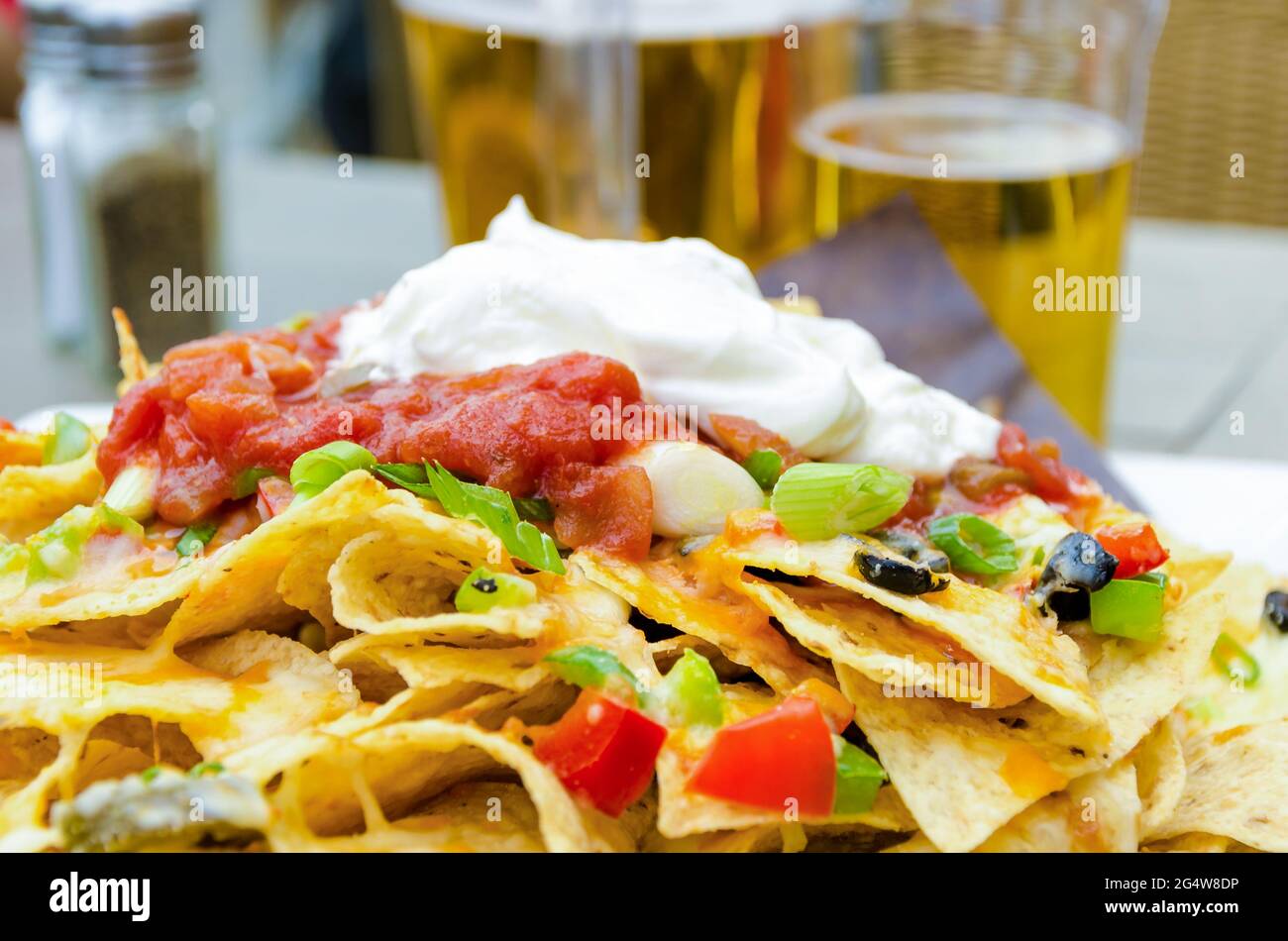 Aperitivo o merienda para beber cerveza en el patio hecho de nachos, crema agria y jalapeños Foto de stock