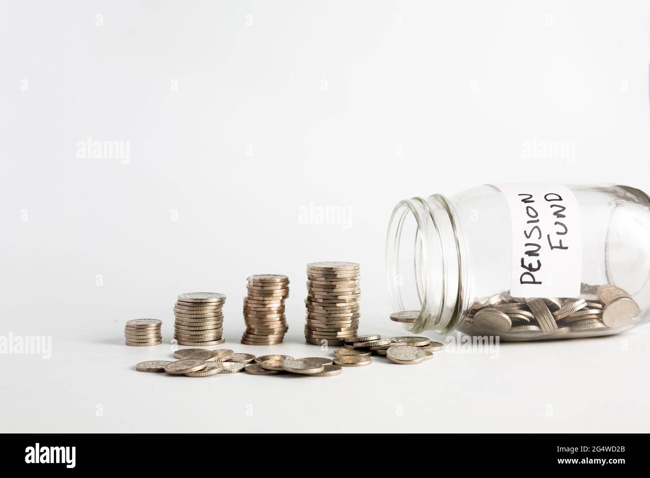 Las monedas se apilaron junto a un medio frasco vacío con monedas y con una etiqueta en dicho fondo de pensiones. Pensiones, finanzas, ahorros, economía, conc. De inversión Foto de stock