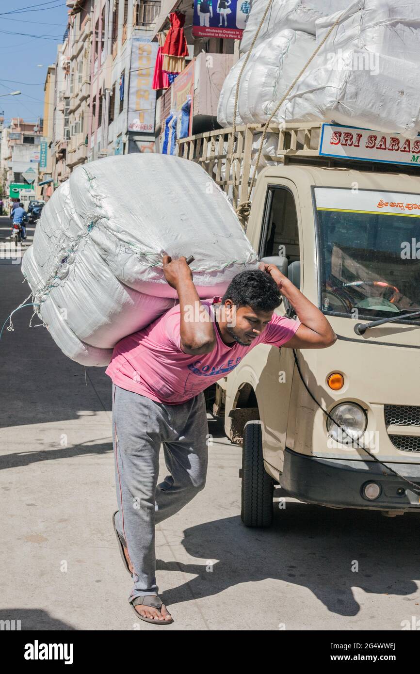 Cargador masculino indio con camisa rosa lleva una carga pesada en la parte de atrás en la calle, Mysore, Karnataka, India Foto de stock