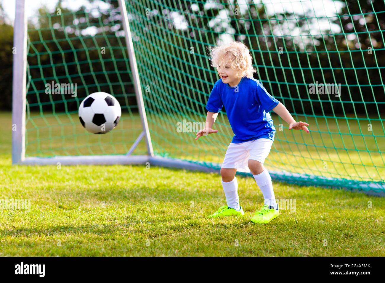 Los niños juegan al fútbol en el campo al aire libre. Los niños anotan meta el partido de fútbol. Niño pequeño pateando pelota. Niño de running con camiseta y tacos