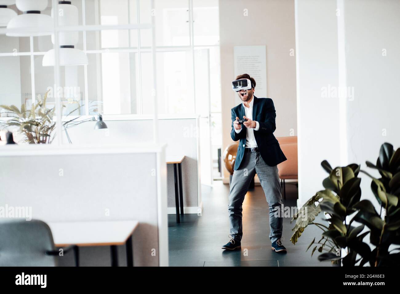 Empresario masculino con auriculares de realidad virtual y controlador de videojuegos jugando en la oficina Foto de stock