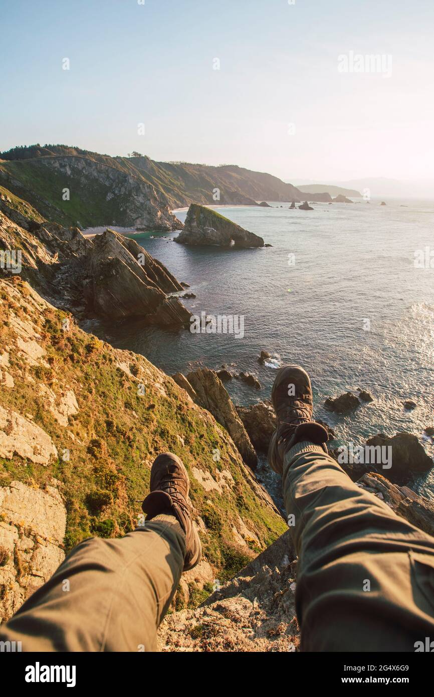 Perspectiva personal del hombre sentado al borde del acantilado costero al atardecer Foto de stock
