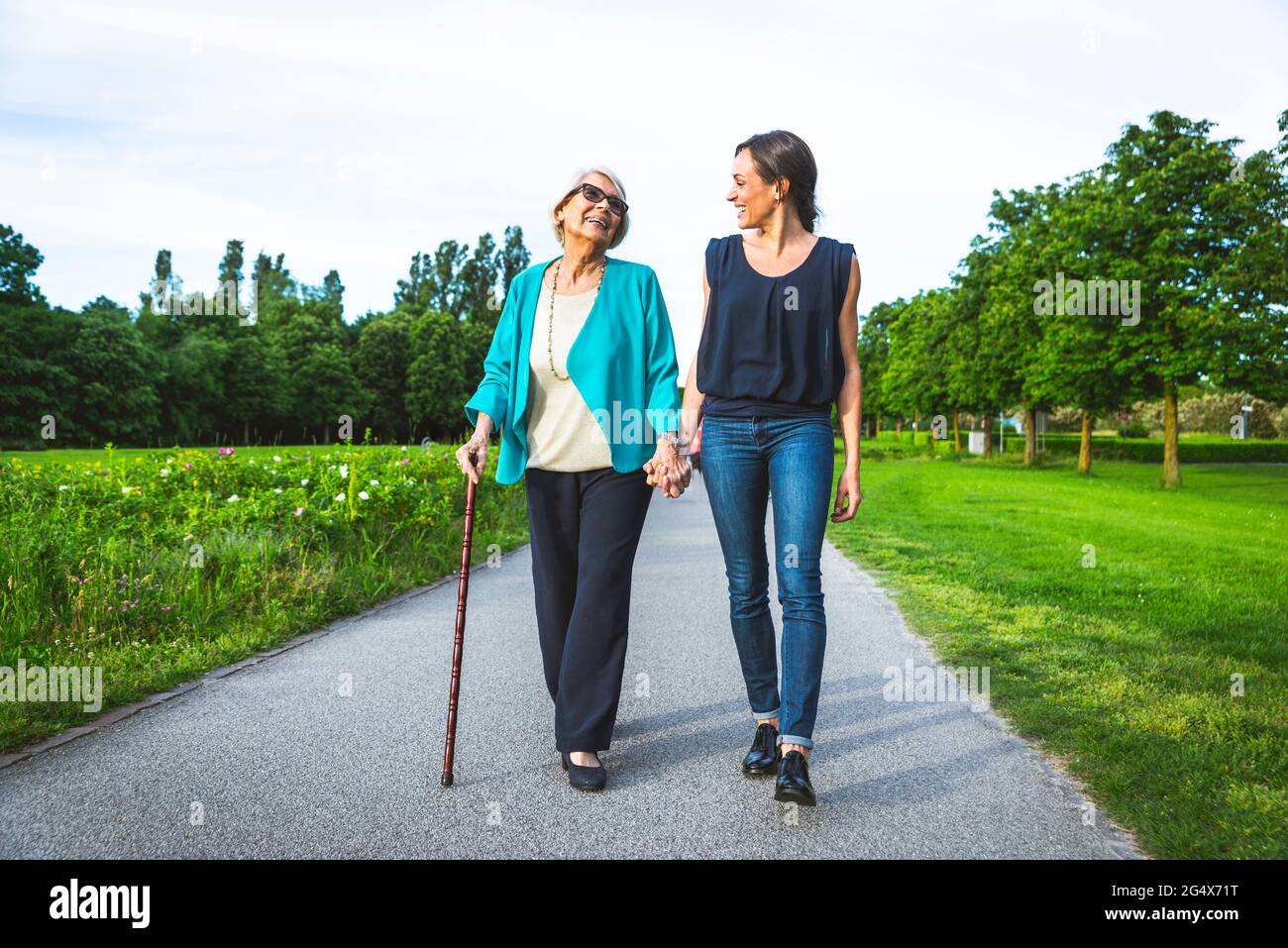 Abuela sonriente sosteniendo mano de nieta mientras caminaba por carretera Foto de stock