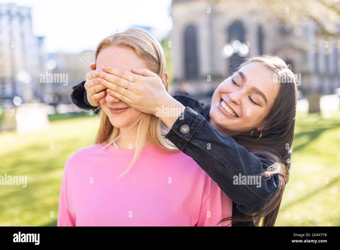 Mujer sonriente cerrando los ojos de una amiga en el parque Foto de stock