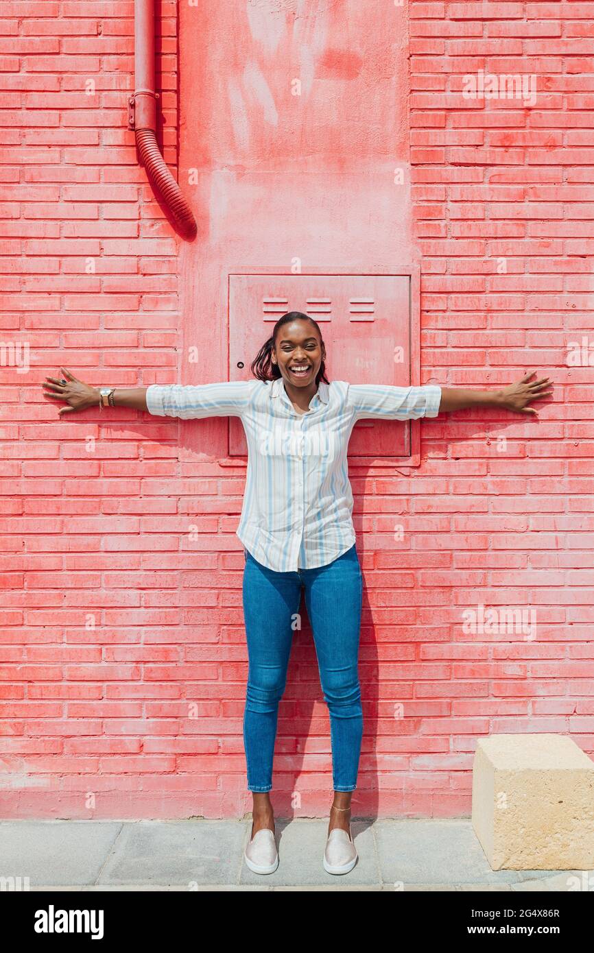 Mujer alegre con los brazos extendidos apoyado en la pared de ladrillo rojo Foto de stock
