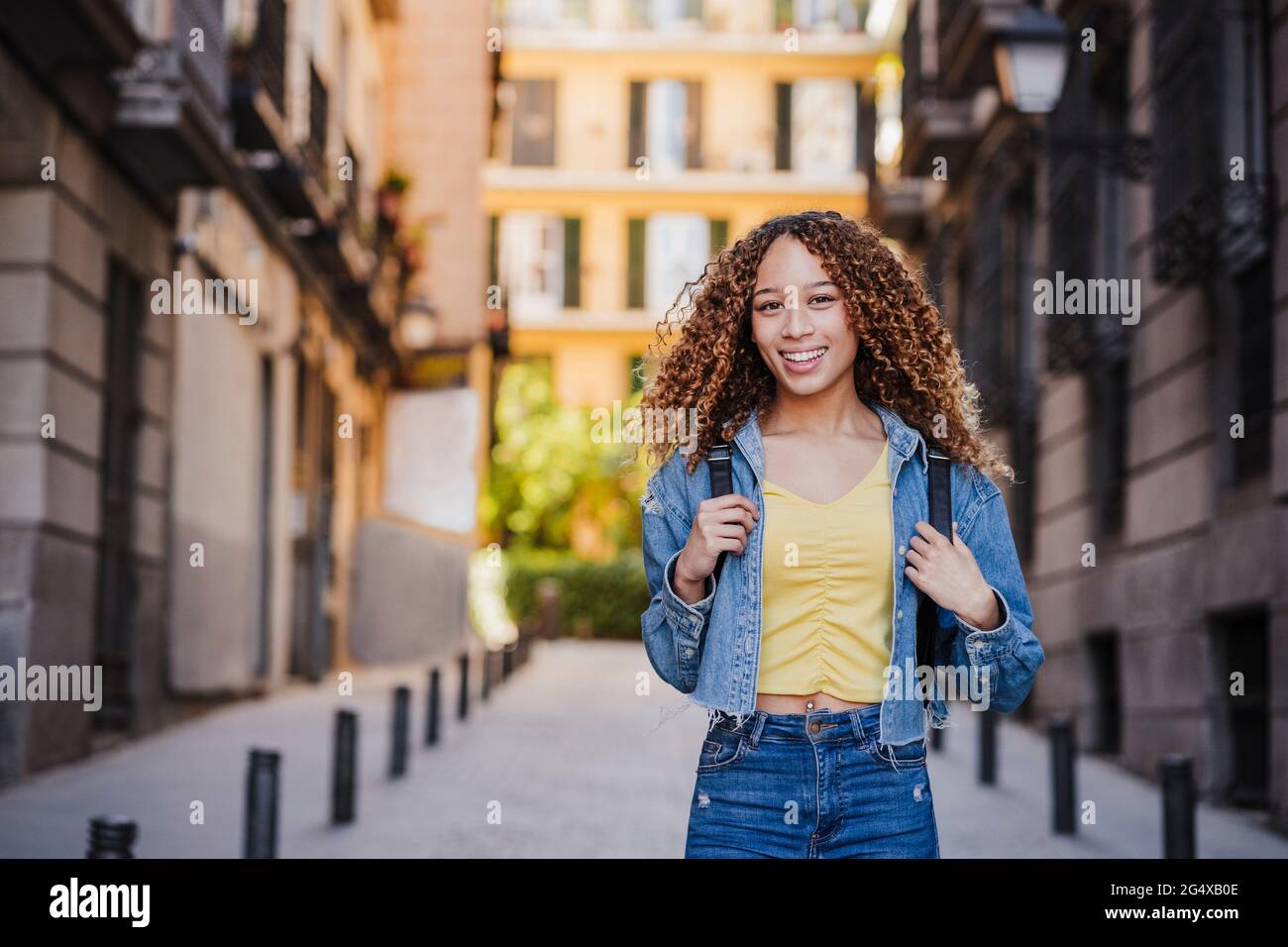 Mujer sonriente con ropa vaquera de pie en un callejón cerca de los  edificios Fotografía de stock - Alamy