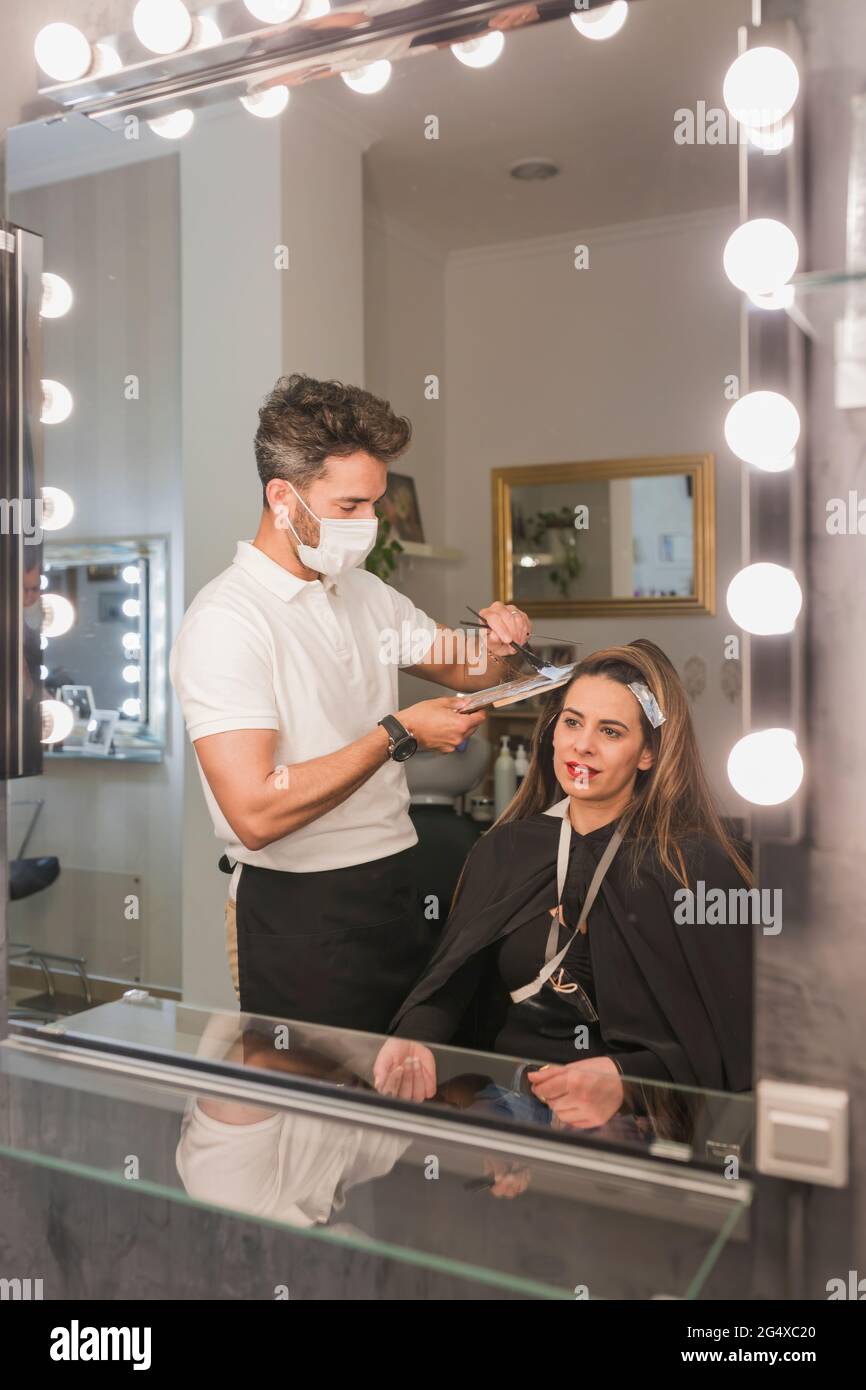 Espejo reflejo de hombre experto teñir el pelo femenino de cliente en el salón Foto de stock