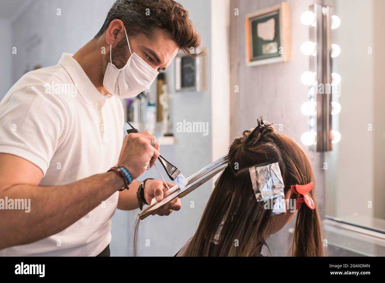 Peluquería masculina con máscara protectora para el cabello del cliente teñido en el salón Foto de stock