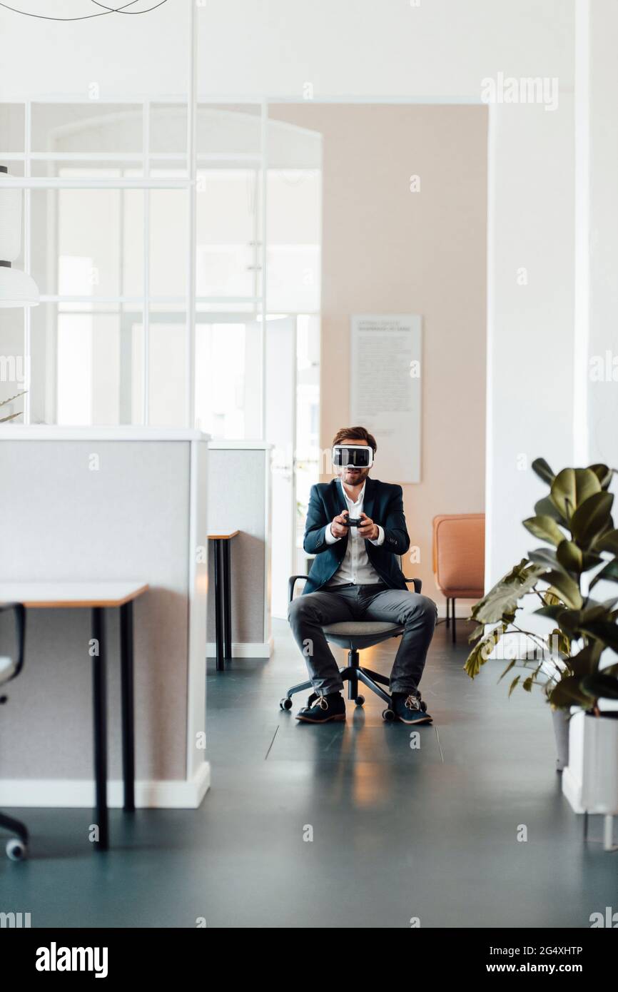 Hombre de negocios con auricular de realidad virtual con controlador de juegos de vídeo en la oficina Foto de stock