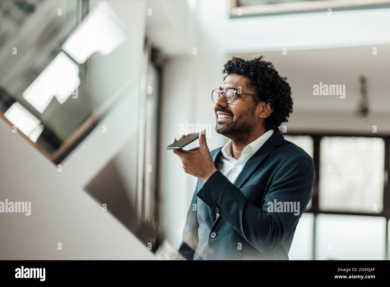 Sonriente hombre profesional hablando a través del altavoz en el teléfono inteligente en la oficina Foto de stock