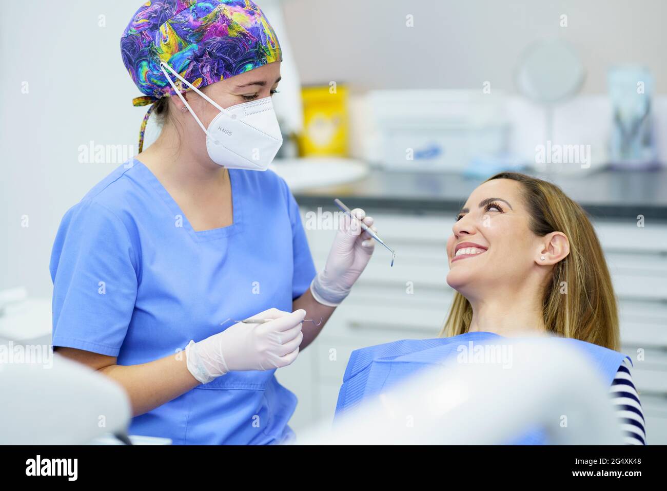 Dentista femenino usando máscara protectora de la cara sosteniendo equipos  dentales mientras que habla con paciente en la clínica Fotografía de stock  - Alamy