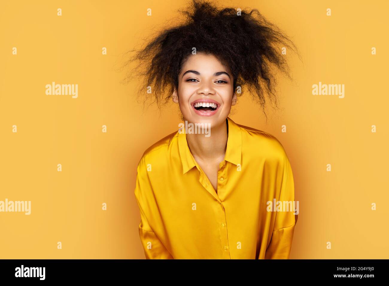 La chica con exceso de alegría no puede dejar de reír. Foto de una niña afroamericana sobre fondo amarillo Foto de stock