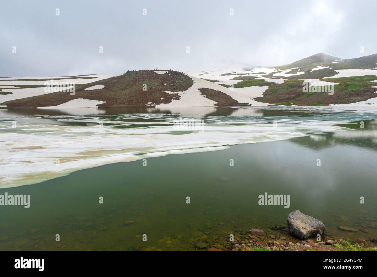 Pintoresco lago Kari en las montañas de Armenia cubiertas de nieve en junio Foto de stock
