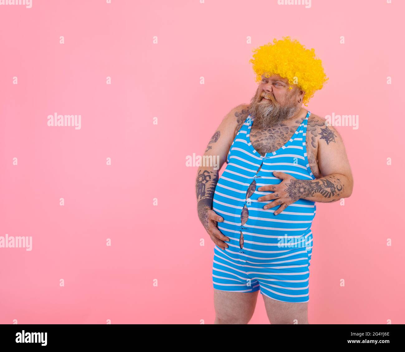 Hombre feliz con peluca amarilla y traje de baño tiene dolor de estómago Foto de stock