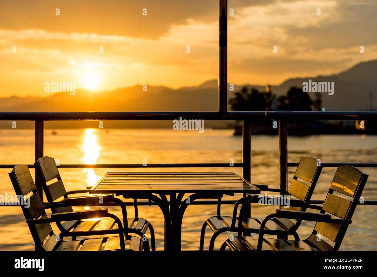 Una mesa en un café junto al mar durante la puesta de sol en naranja Foto de stock