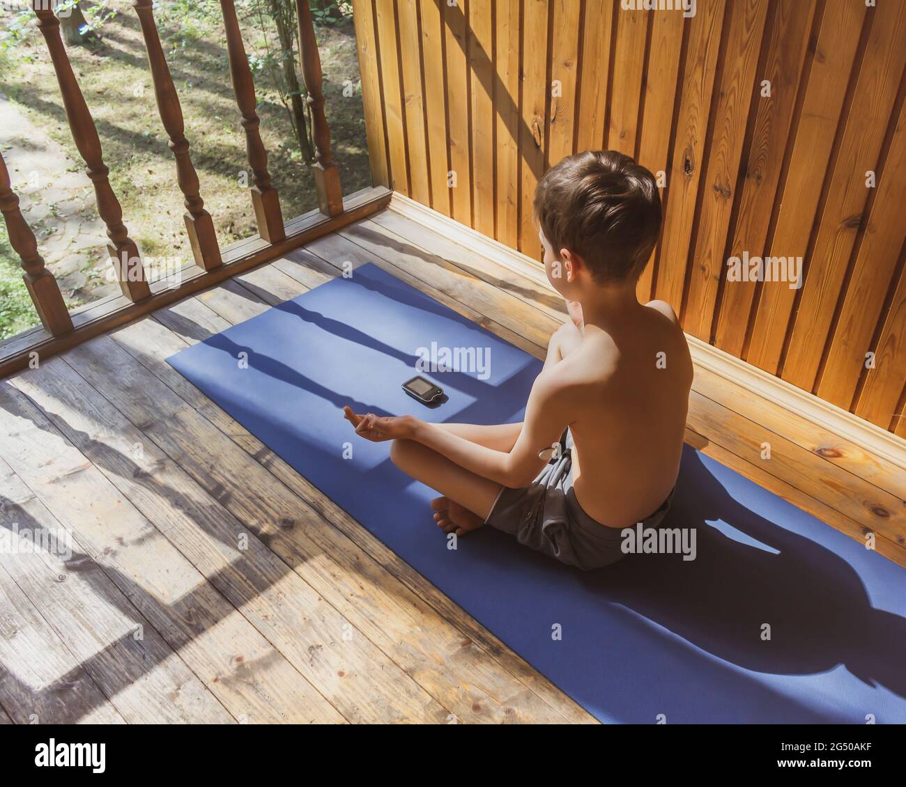Un niño diabético hace yoga al aire libre con un dispositivo de control glucémico. Concepto de vida de un niño y deporte con diabetes y control glucémico. Verano Foto de stock