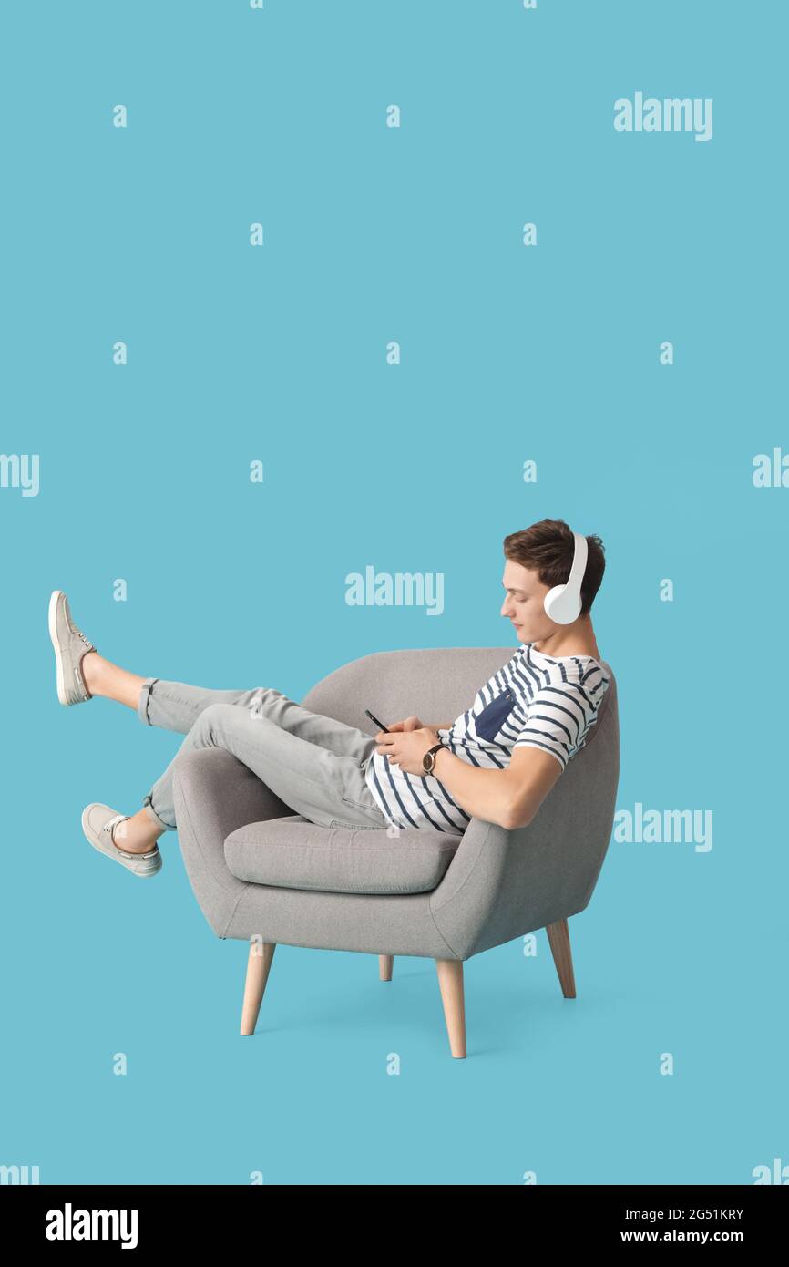 Hombre joven escuchando música sentado en el sillón sobre fondo de color  Fotografía de stock - Alamy