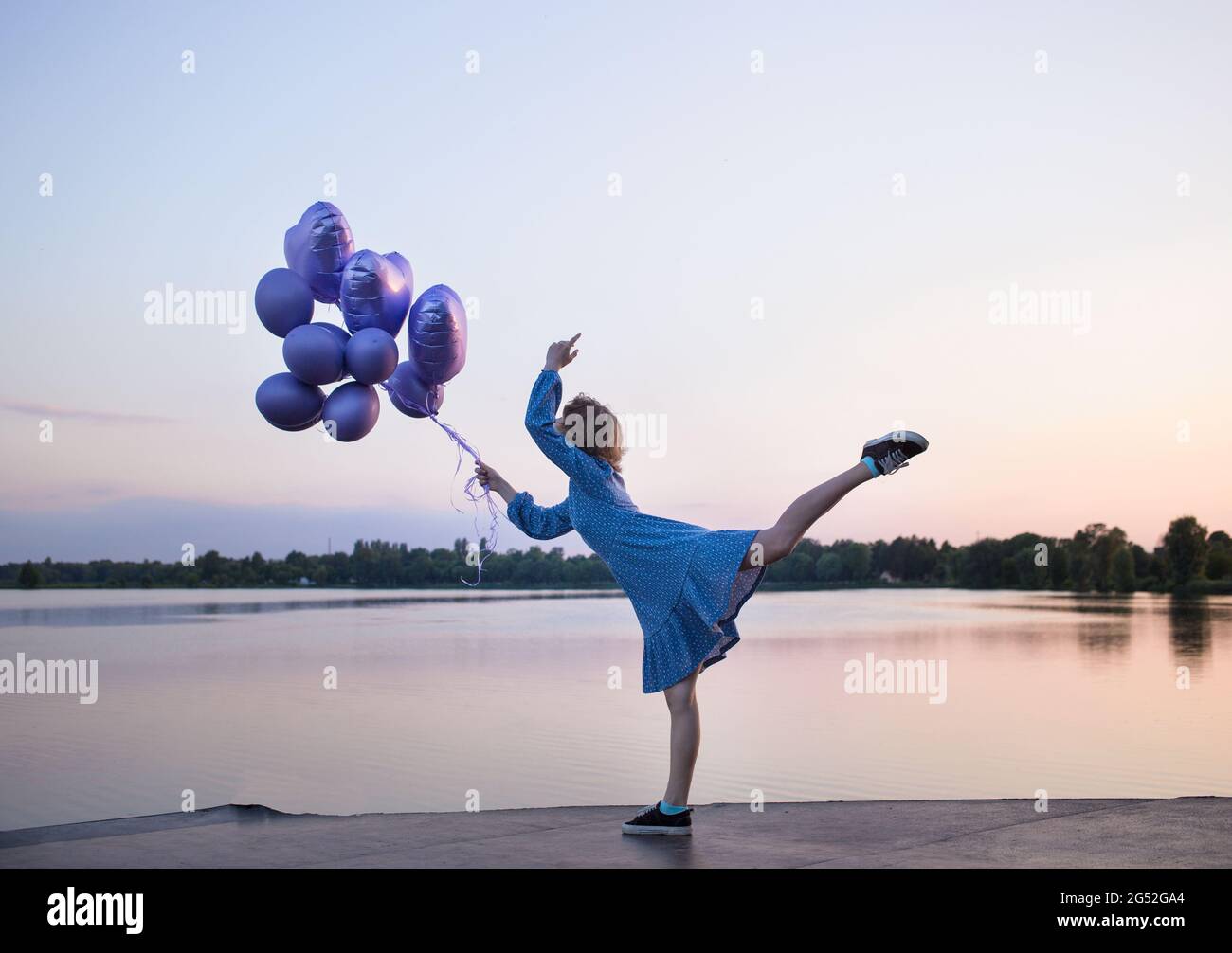 joven mujer esbelta irreconocible, levantando con gracia su pierna, se  encuentra cerca del lago al atardecer, sosteniendo un montón de globos en  la mano. fantasías, sueños, positi Fotografía de stock - Alamy
