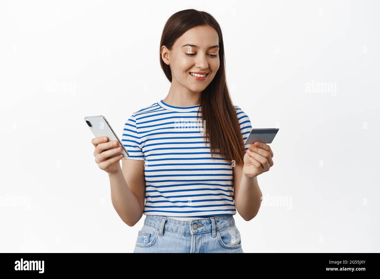 Compras en línea. Mujer joven que paga con tarjeta de crédito y teléfono móvil, sonriendo y mirando relajado, la compra smth en tienda de Internet, comprando adentro Foto de stock