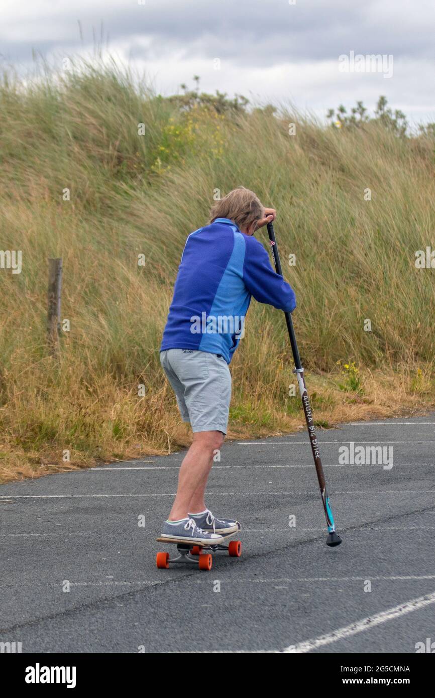 Southport, Merseyside. Clima del Reino Unido, 26 de junio de 2021; colores brillantes en un día aburrido, ya que los residentes locales hacen ejercicio temprano por la mañana (ejercicio de cuerpo entero) en el paseo marítimo del complejo. John 74, que sufre de la enfermedad de las neuronas motoras y un jubilado los agricultores ejercitan los músculos inusuales por el skateboarding de tierra y se empuja a sí mismo a lo largo del paseo marítimo. El remo en tierra es uno de los deportes de tabla más accesibles para personas de todas las edades, pero tiene un pequeño seguimiento. Crédito: MediaWorldImages/AlamyLiveNews Foto de stock