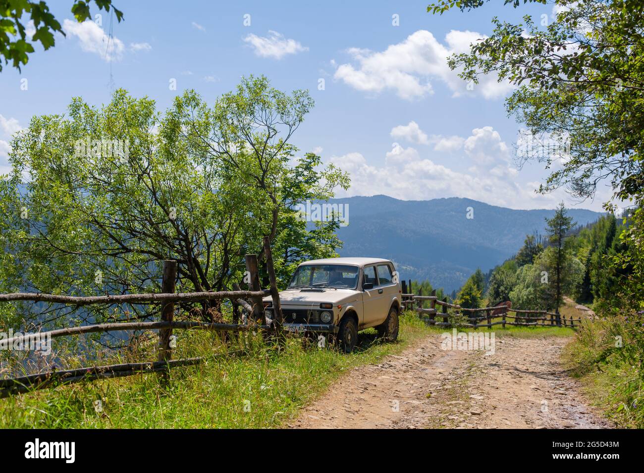 Viejo jeep ruso estacionado al lado de la valla de madera en la carretera sucia de montaña. Día de verano. Excursión a la montaña. Foto de stock