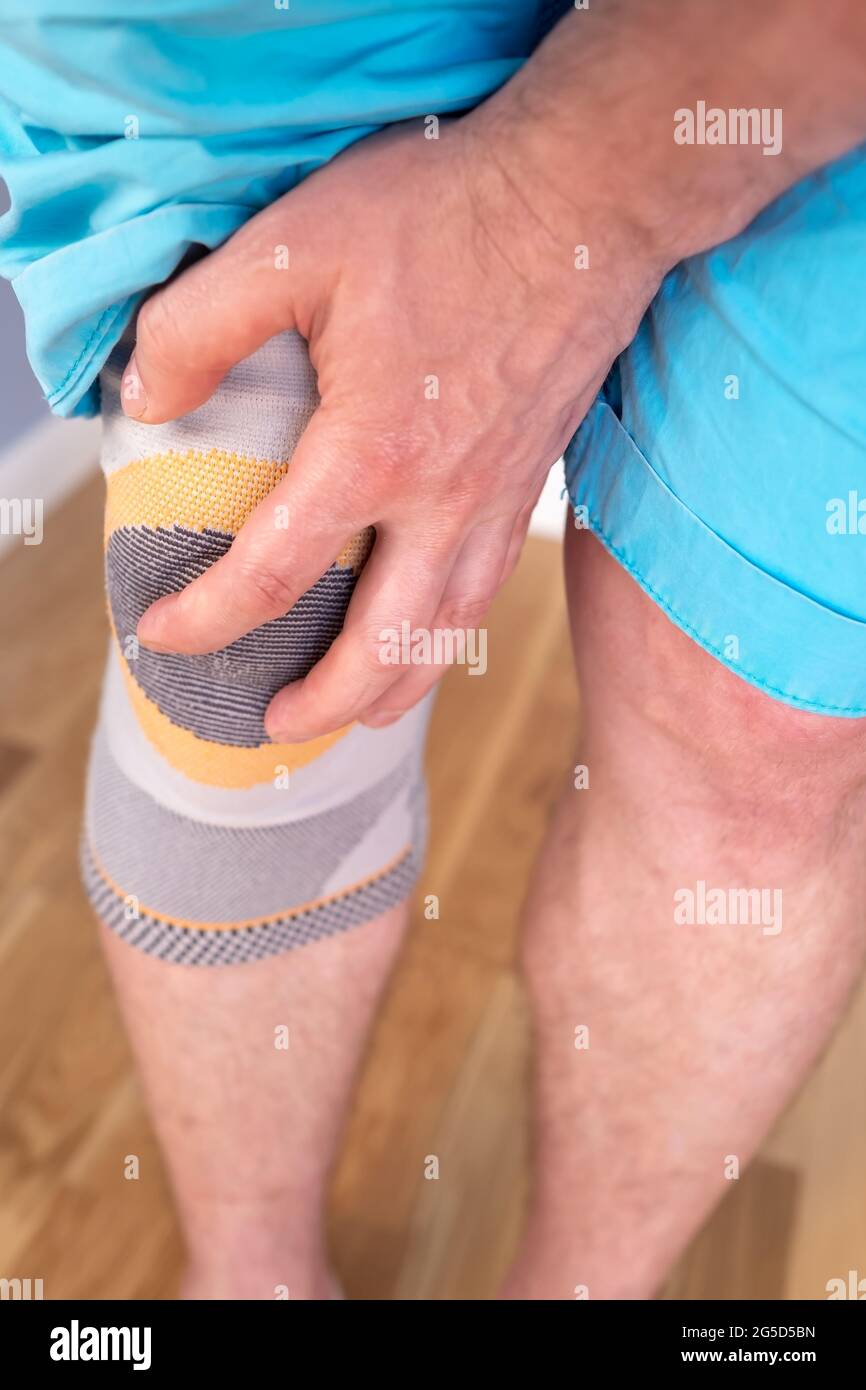 El hombre sostiene la mano para una articulación de rodilla lesionada con un fijador estabilizador especial, contra el fondo del parquet. Vista superior. Foto de stock