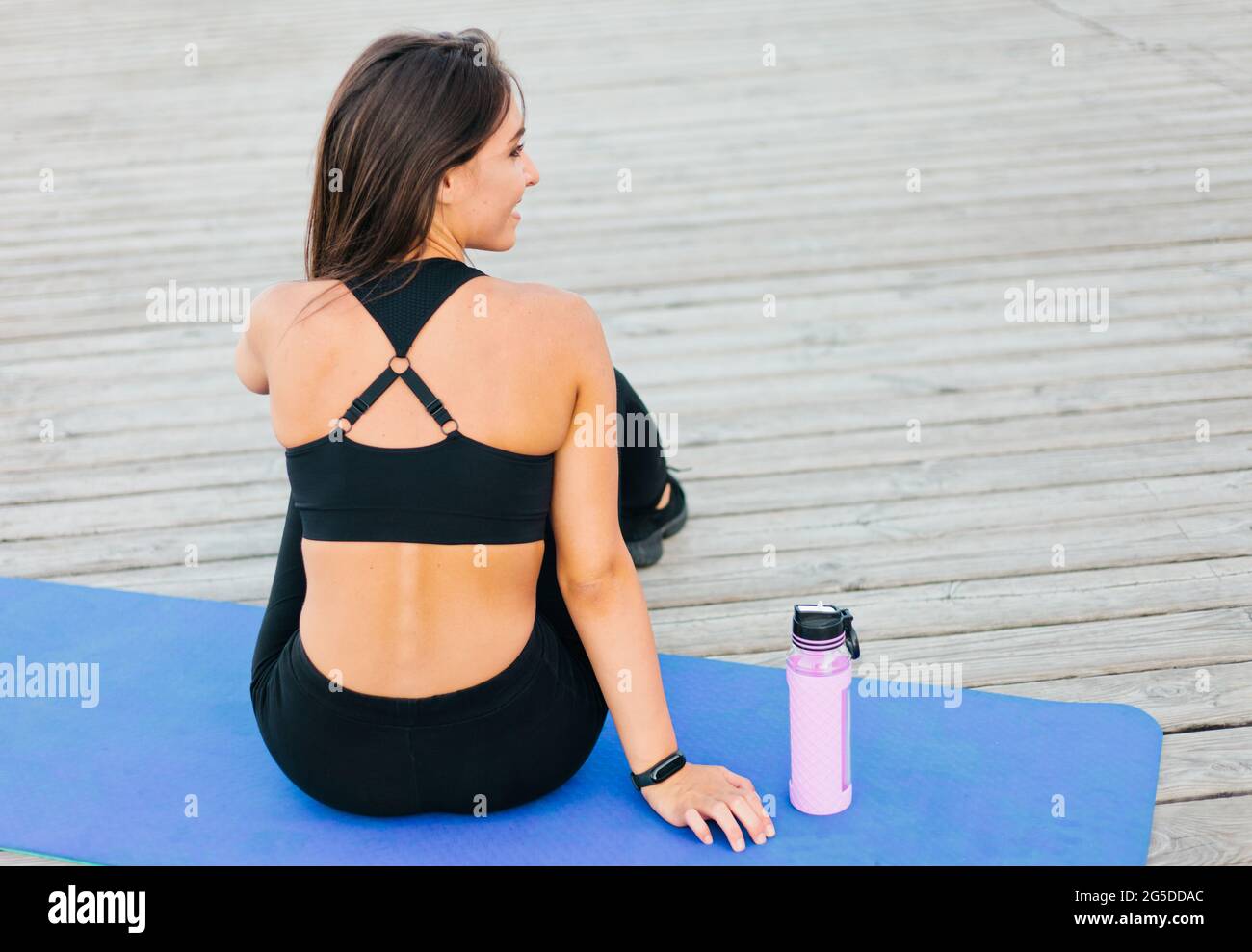 Mujer ajustada ropa deportiva sentada en una colchoneta de yoga al aire libre. Vista desde la parte Fotografía de stock - Alamy