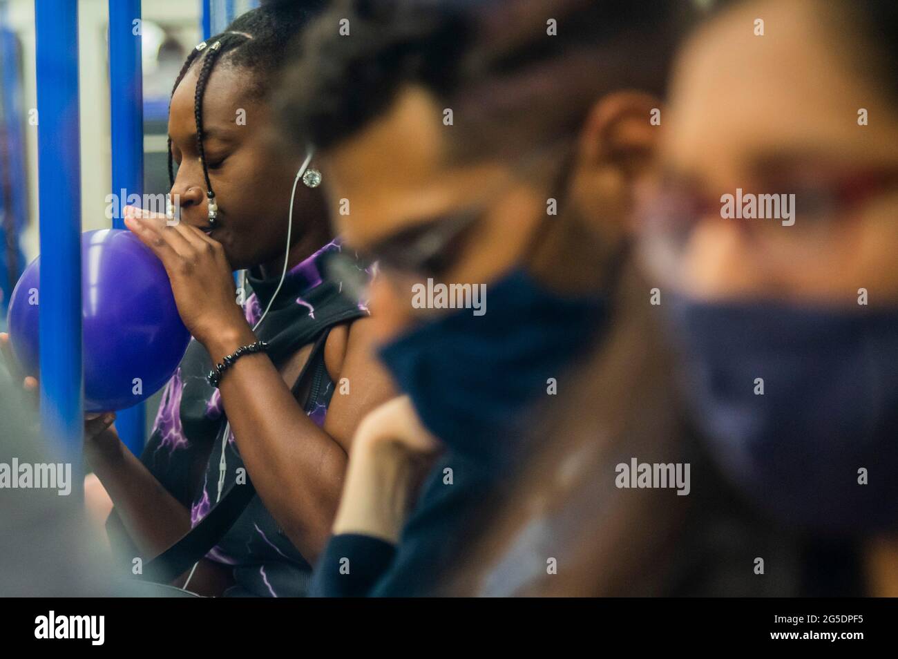 Londres, Reino Unido. 26th de junio de 2021. Una mujer negra desenmascarada se filma y chupa un balón (presumiblemente lleno de óxido nitroso) - el metro está ocupado y muchas personas no usan máscaras ya que nos acercamos al final de las restricciones del coronavirus. Crédito: Guy Bell/Alamy Live News Foto de stock