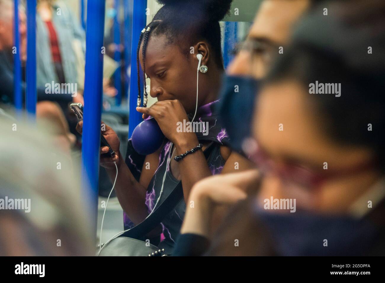 Londres, Reino Unido. 26th de junio de 2021. Una mujer negra desenmascarada se filma y chupa un balón (presumiblemente lleno de óxido nitroso) - el metro está ocupado y muchas personas no usan máscaras ya que nos acercamos al final de las restricciones del coronavirus. Crédito: Guy Bell/Alamy Live News Foto de stock