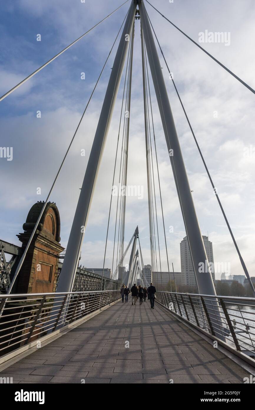 Vea a lo largo del puente Golden Jubilee junto al puente Hungerford sobre el río Támesis en Londres, Inglaterra mostrando los pilones de acero y la gente en la cubierta Foto de stock