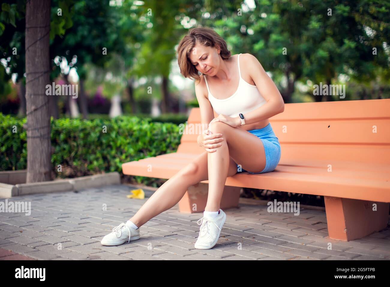 Dolor de rodilla. Mujer con lesión en la rodilla sentada en el banco al aire libre. Concepto de salud y estilo de vida Foto de stock