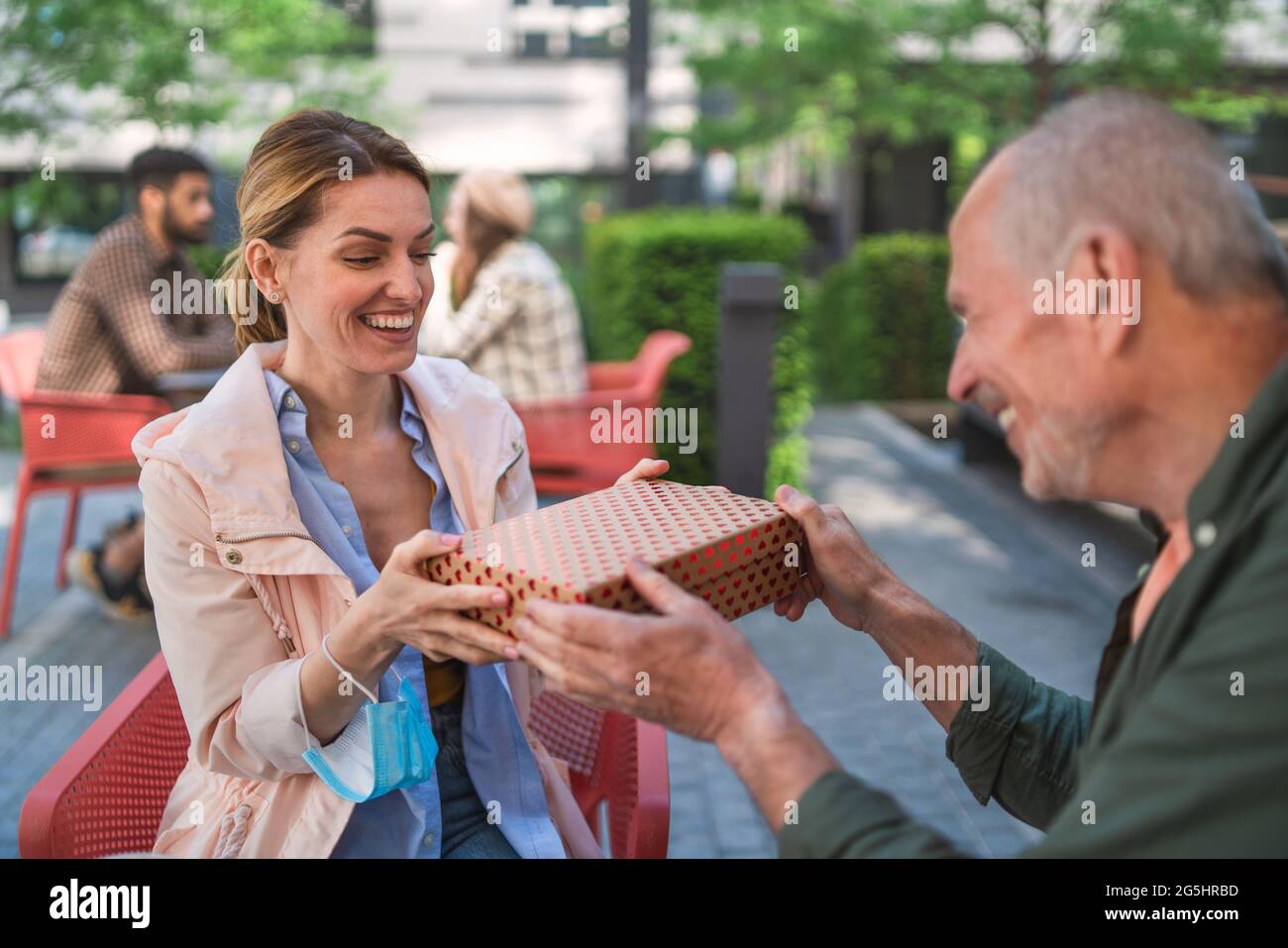 Padre mayor que da el regalo a los adultos daugther al aire libre en la ciudad, reuniéndose en un concepto de café. Foto de stock