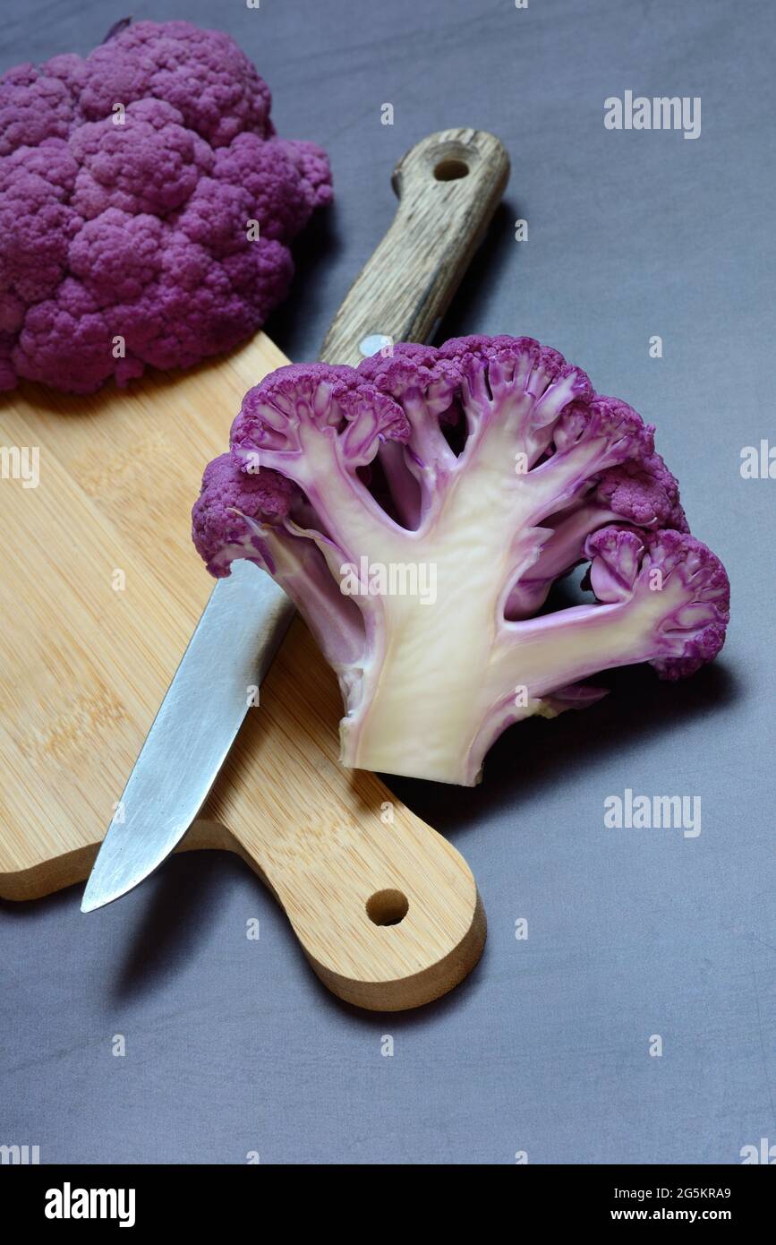 Coliflor púrpura por la mitad sobre tabla de madera con cuchillo de cocina Foto de stock
