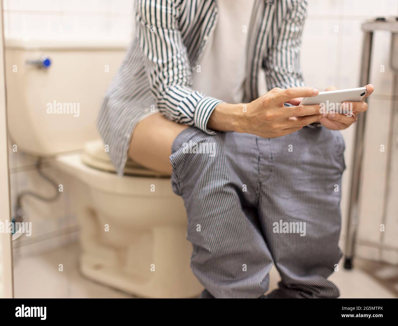 el hombre tiene diarrea en el baño, usando el teléfono móvil horizontalmente para jugar a juegos móviles/ver videos en el teléfono móvil Foto de stock