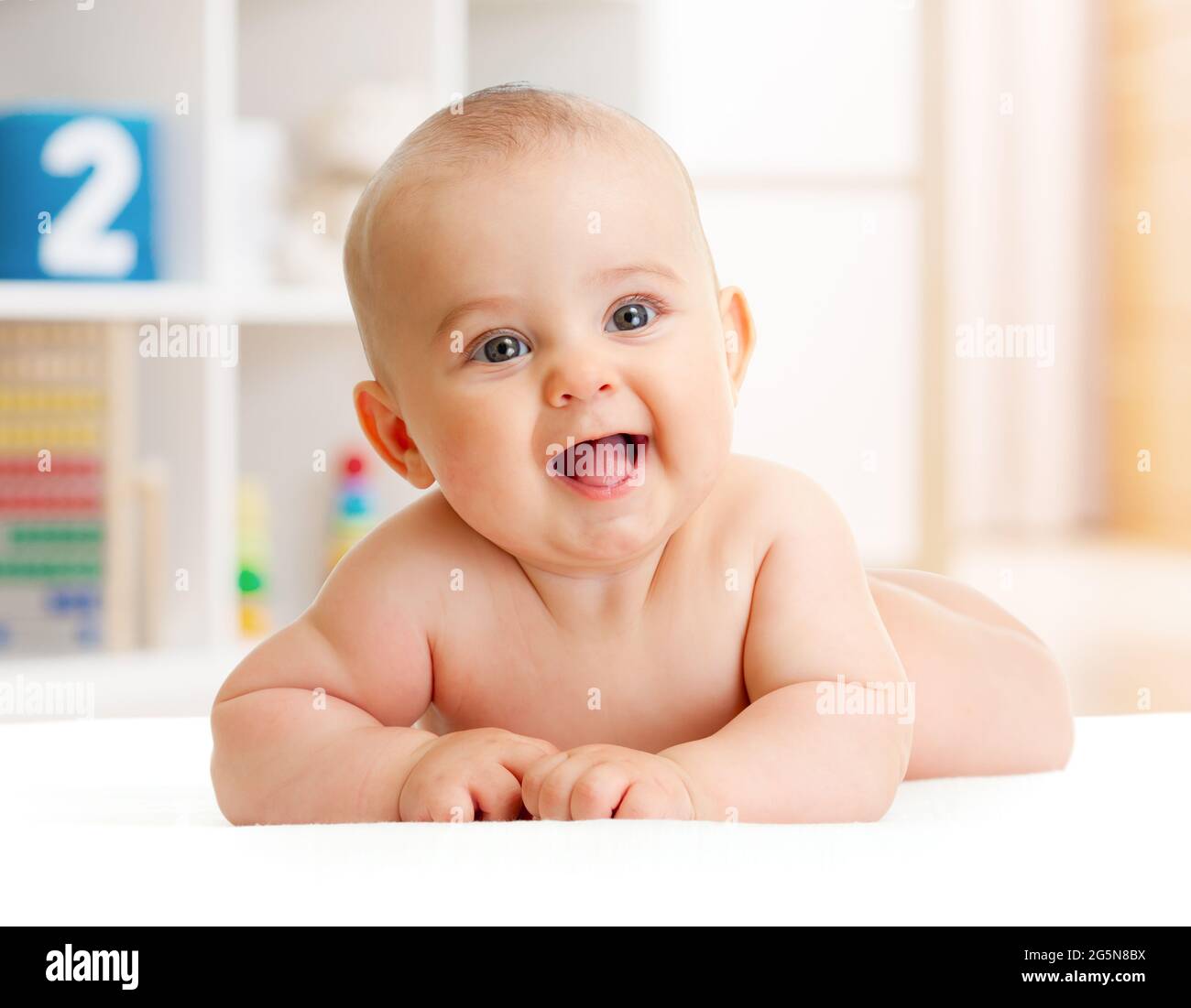 Adorable bebé sonriente tumbado en la habitación Foto de stock