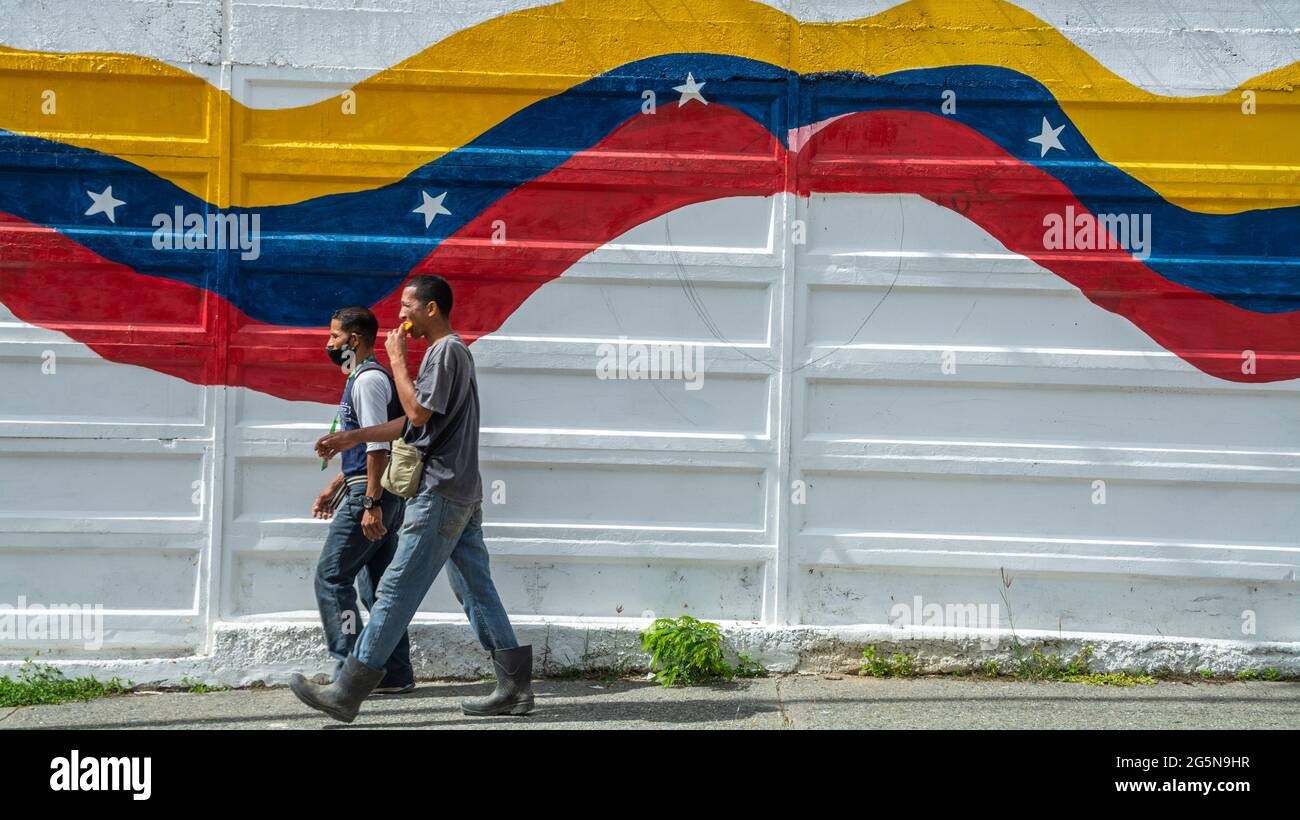 Dos hombres caminan por una calle de Caracas en el barrio de Las Mayas, mientras uno come mango. Foto de stock
